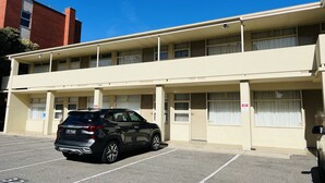 Um motel de dois andares com quartos numerados, um estacionamento e um SUV preto estacionado na frente.
