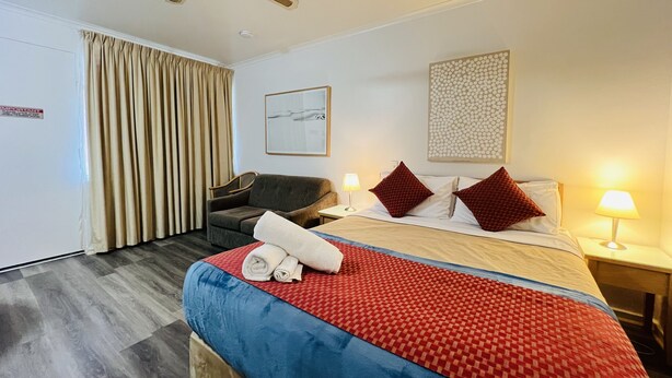 Quarto de hotel com cama, escrivaninha, cadeira, ventilador de teto e janela com cortinas.