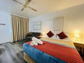Une chambre d’hôtel équipée d’un lit, d’un bureau, d’une chaise, d’un ventilateur de plafond et d’une fenêtre avec des rideaux.