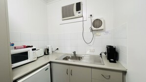 Uma kitchenette compacta com micro-ondas, chaleira, máquina de café e um pequeno frigorífico.