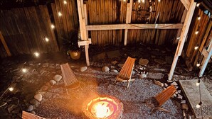 Un espacio de estar al aire libre, circular, con un brasero en el centro, rodeado de rocas y bancos de madera.