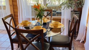 Interior de madera con una mesa de comedor preparada para cuatro personas, rodeada de sillas.