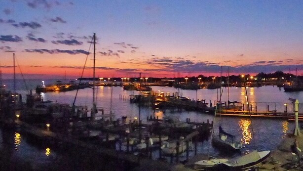 Un puerto deportivo al atardecer con barcos amarrados y luces que se reflejan en el agua.
