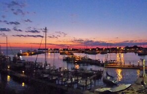 A marina at dusk with boats docked and lights reflecting on the water.