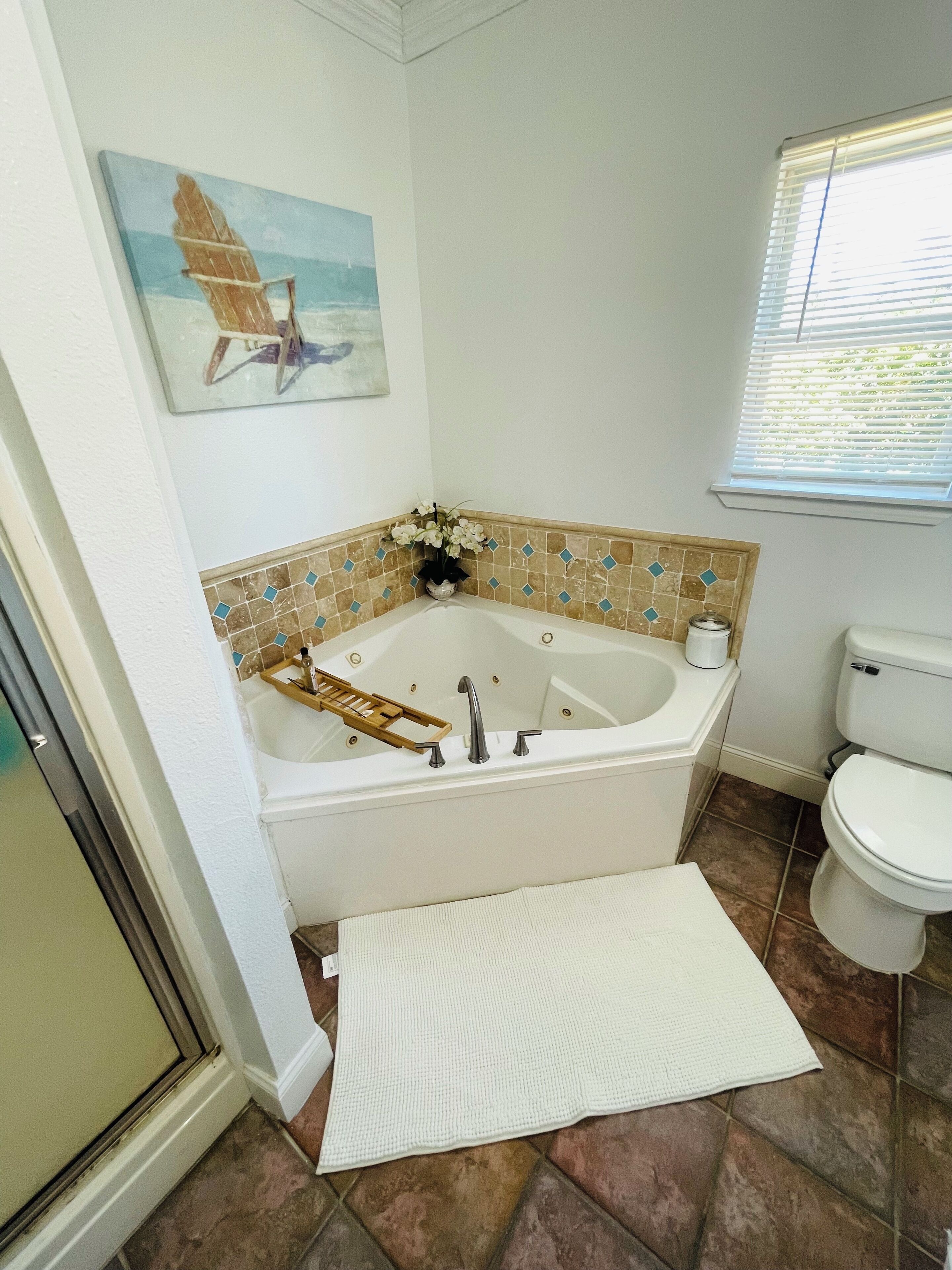 A bathroom with a bathtub, toilet, and a window with blinds.