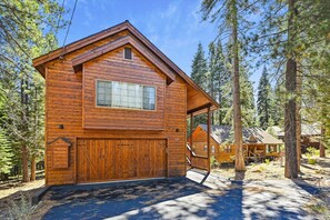 Set amidst the forest, this lodge features a large garage door and a pitched roof with a front window.