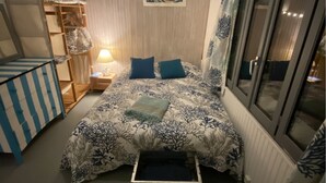 A bedroom with a bed, a wardrobe, a nightstand, a lamp, and a window.