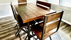 Een eetgedeelte met een houten tafel en stoelen, een hanglamp en een schilderij aan de muur.