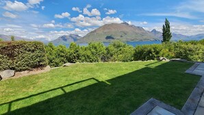 Un jardí ben cuidat amb un camí de pedra que condueix a una zona d'estar, envoltat de vegetació abundant i amb un paisatge de muntanyes al fons.