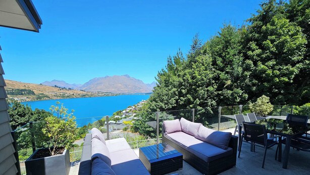 Eine Außenpatio mit einer Couch, Stühlen und einem Tisch mit Blick auf einen See und Berge.