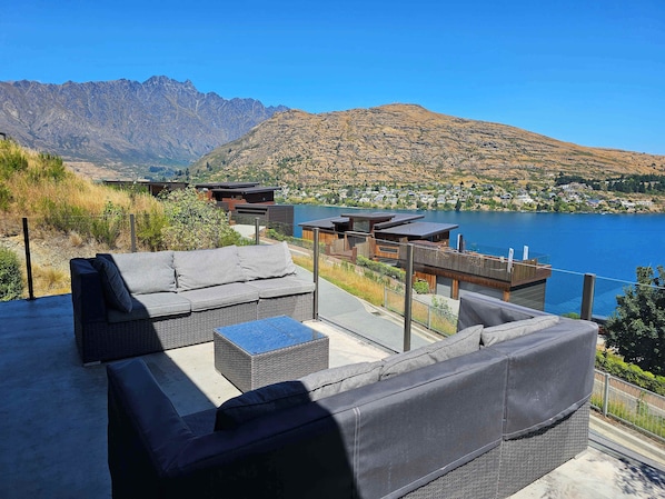 A modern outdoor seating area with a sofa and a small table, overlooking a lake and mountains.