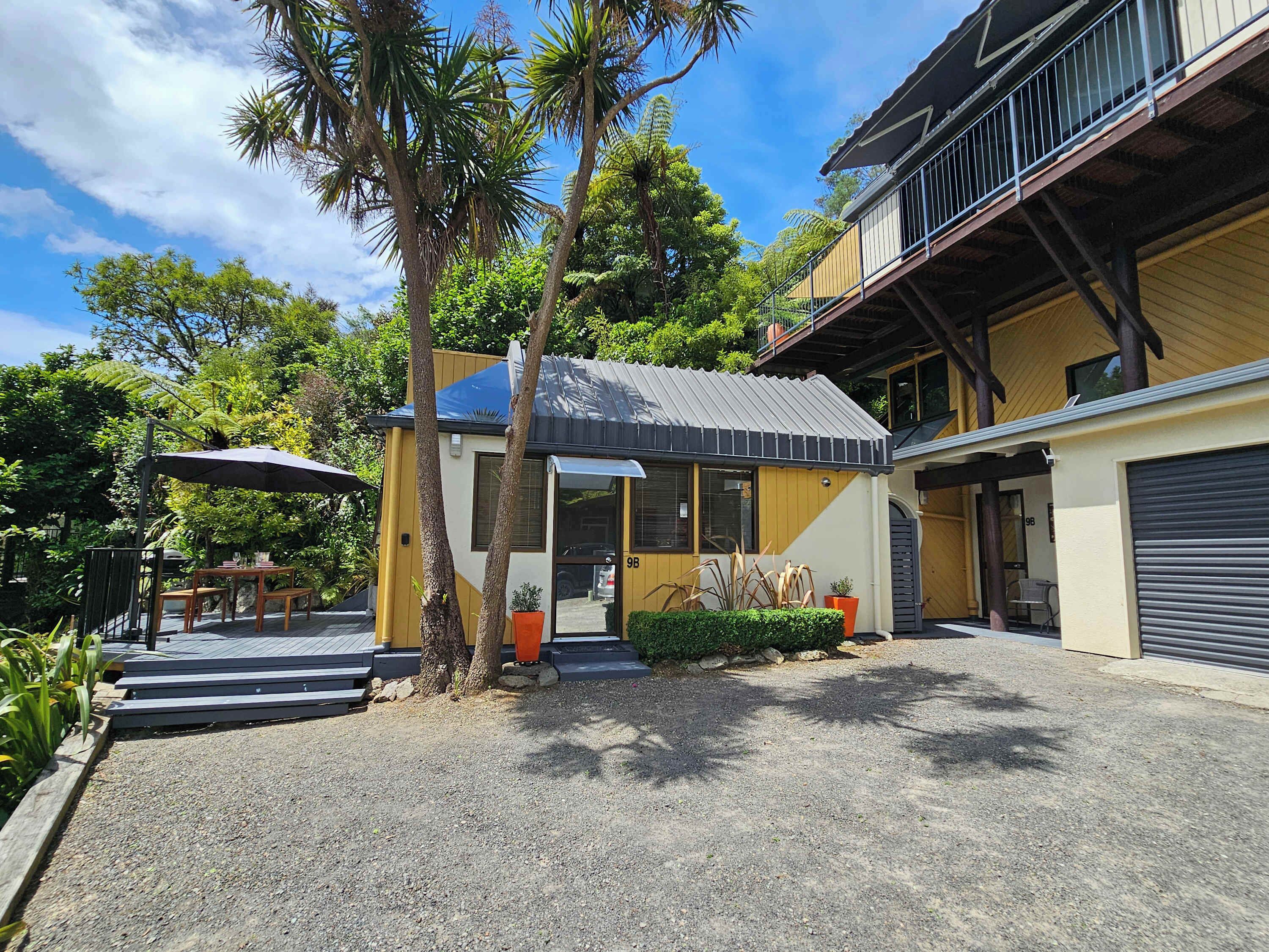 Um edifício de dois andares com área de estar coberta ao ar livre, garagem e entrada pavimentada.