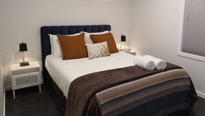 Ein Hotelzimmer mit einem Bett, zwei Nachttischen, einem Fenster mit Jalousien und einem Deckenventilator.