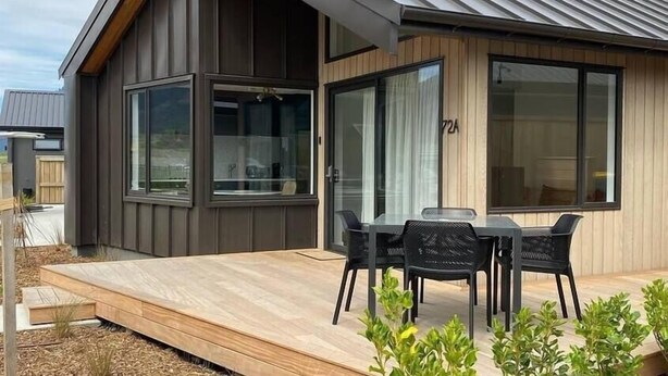 Ein modernes Haus mit einer großen Terrasse, einem Essbereich mit Stühlen und einem großen Fenster.