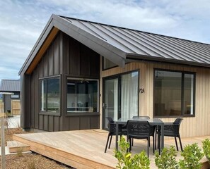 Et moderne hus med stor terrasse, spiseplads med stole og stort vindue.