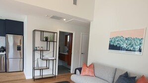 Ein modernes Wohnzimmer mit grauem Sofa, einem schwarzen Couchtisch und einer Küche im Hintergrund.