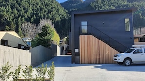 Un edificio moderno con fachada de madera, una escalera y un coche estacionado al frente.