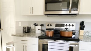 A kitchen with white cabinets, a stainless steel stove, a microwave, and a trash can.