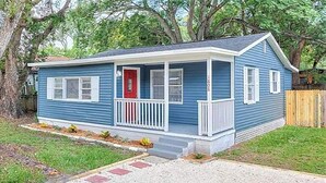 A single-story house with a front porch, a red door, and a small front yard.