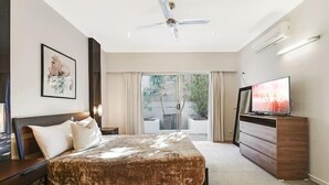 Une chambre à coucher comprenant un lit, une commode, un téléviseur, un ventilateur de plafond et une fenêtre donnant sur un paysage verdoyant.