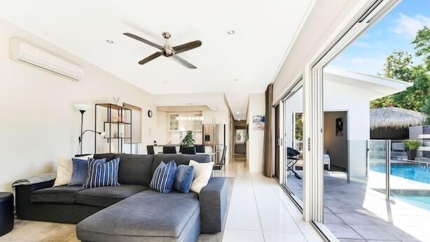 Un salon moderne avec un canapé d’angle, un ventilateur de plafond et une vue sur une piscine.