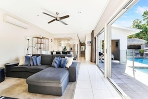 A modern living room with a sectional sofa, a ceiling fan, and a view of a swimming pool. - TWELVE @ 12 Private Central Maroochydore (Maroochydore)