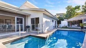 Une maison moderne dotée d’une piscine, d’un patio couvert et d’une structure surmontée d’un toit de chaume.
