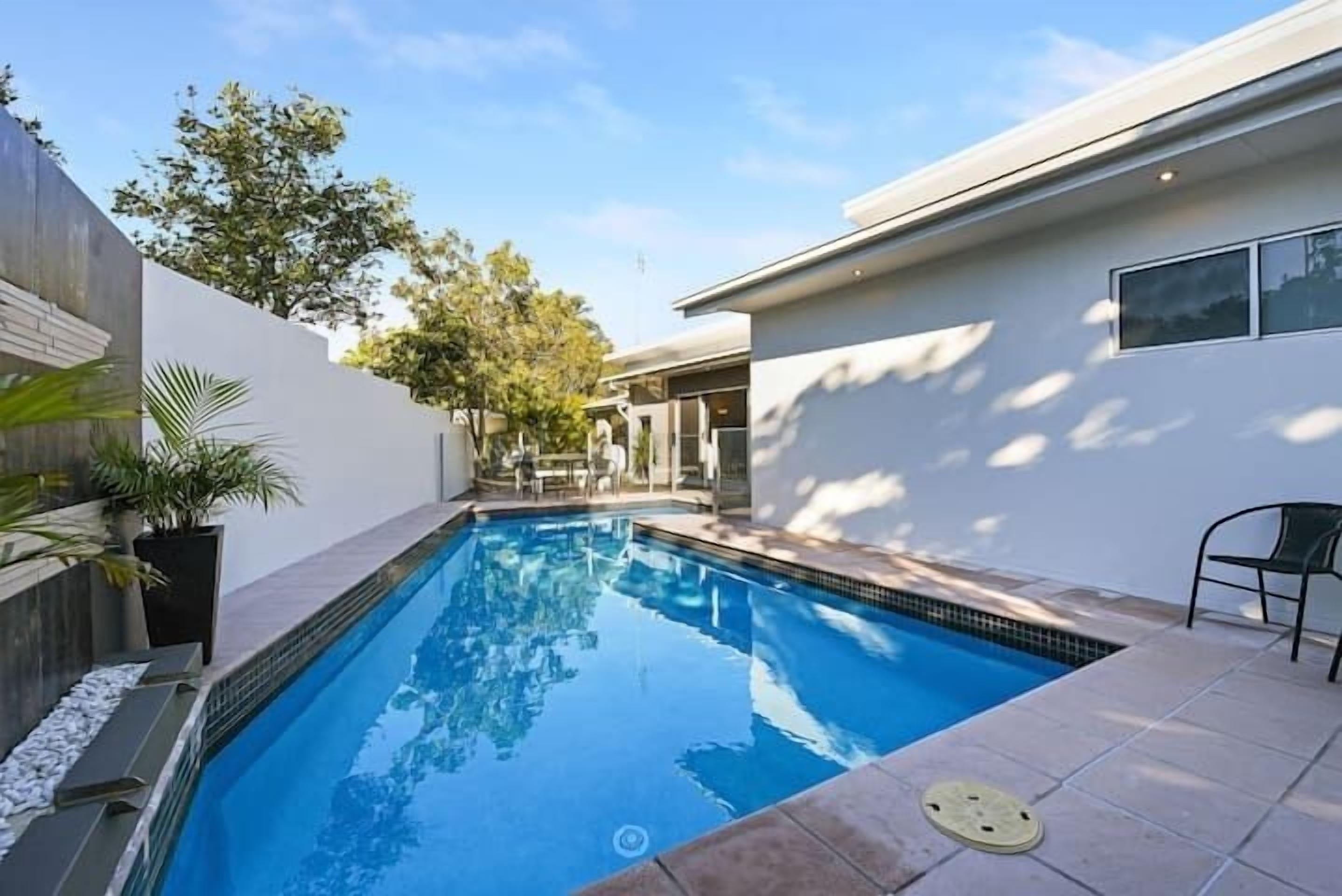 A swimming pool with a tiled deck, a potted plant, and a chair.