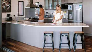 A modern kitchen with a central island, stainless steel appliances, and wooden flooring. - Wilderness House l Infinity Pool & Views (Kulangoor)