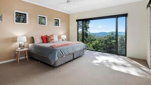 A bedroom with a bed, two bedside tables, a ceiling fan, and a large window with a view of greenery. - Wilderness House l Infinity Pool & Views (Kulangoor)