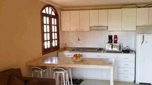 A kitchen with white cabinets, a marble countertop, a coffee maker, and a refrigerator. - Hospedagens La Fazenda Canoa Quebrada (Aracati)