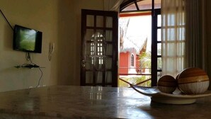 A room with a television on the wall, a wooden door, and a view of the outside. - Hospedagens La Fazenda Canoa Quebrada (Aracati)