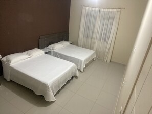 A room with two single beds, a wooden headboard, a curtain, and tiled flooring. - Hospedagens La Fazenda Canoa Quebrada (Aracati)