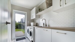 A modern kitchen with white cabinetry, a built-in washing machine, a sink, and a window overlooking a garden.