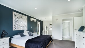 A modern bedroom with a bed, bedside tables, a dresser, and a shower area.