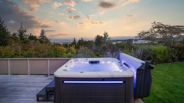 A hot tub on a wooden deck with a view of trees and a cloudy sky.