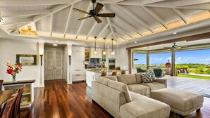 A spacious living area with a large sectional sofa, wooden flooring, and a ceiling fan. - Gorgeous Poipu Villa with Pool & Spa + Ocean Views (Koloa)