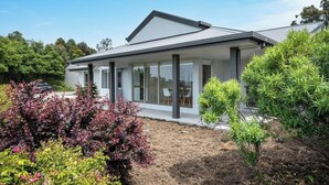 A modern house with a large glass window, surrounded by well-maintained shrubs and a clear sky.