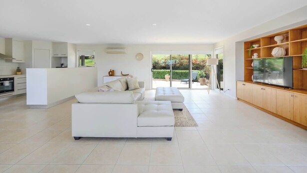 A modern living room with a white sectional sofa, a wooden entertainment unit, and a large TV.