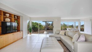 A modern living room with a sectional sofa, a flat-screen TV on a wooden cabinet, and a large sliding glass door leading to an outdoor area.