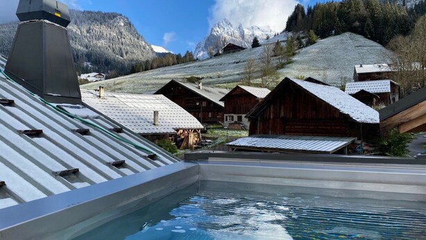 A hot tub with a view of a mountain range and wooden cabins.