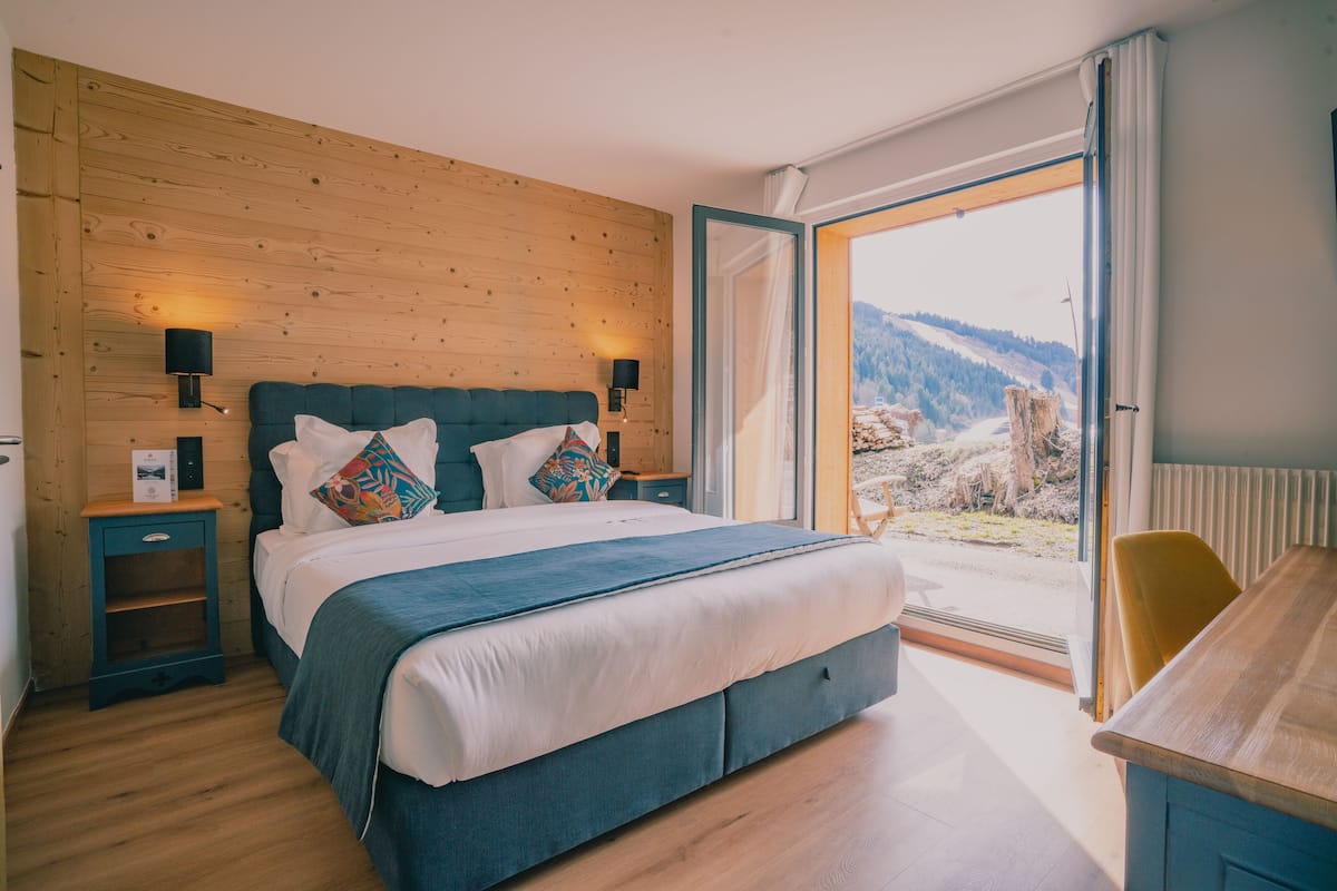 Ein Schlafzimmer mit einem großen Bett, Holzwandverkleidung, einem Nachttisch, einem Schreibtisch und Blick auf eine Berglandschaft.