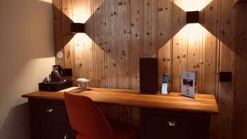 A wooden desk with a coffee maker, a smartphone, and a water bottle. There is a red chair and a cabinet with a handle.