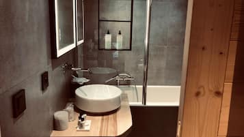 A modern bathroom with a round sink, a mirror, and a shower area.
