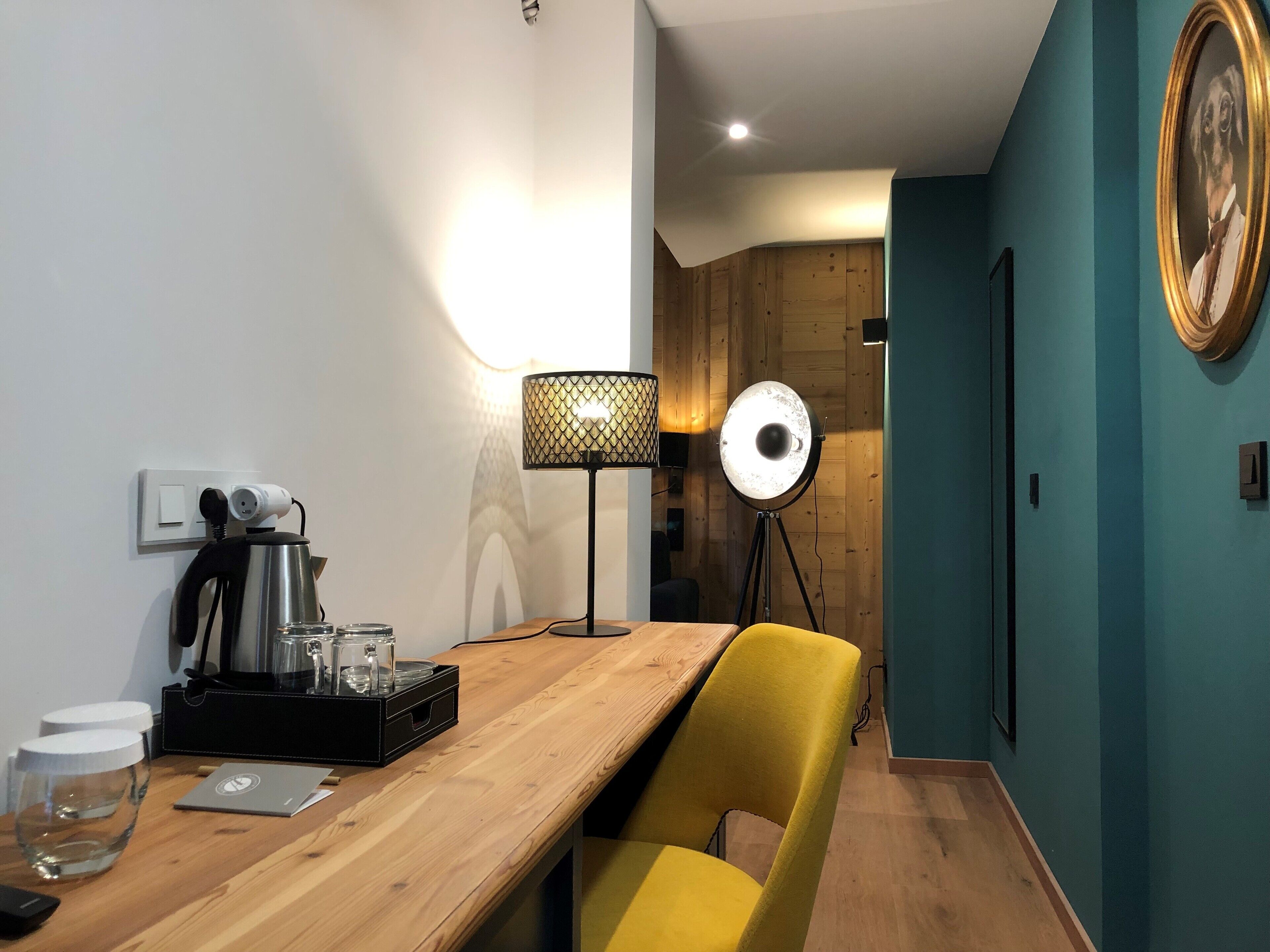 Une chambre moderne avec un bureau en bois, une chaise jaune, une lampe et un tableau encadré au mur.