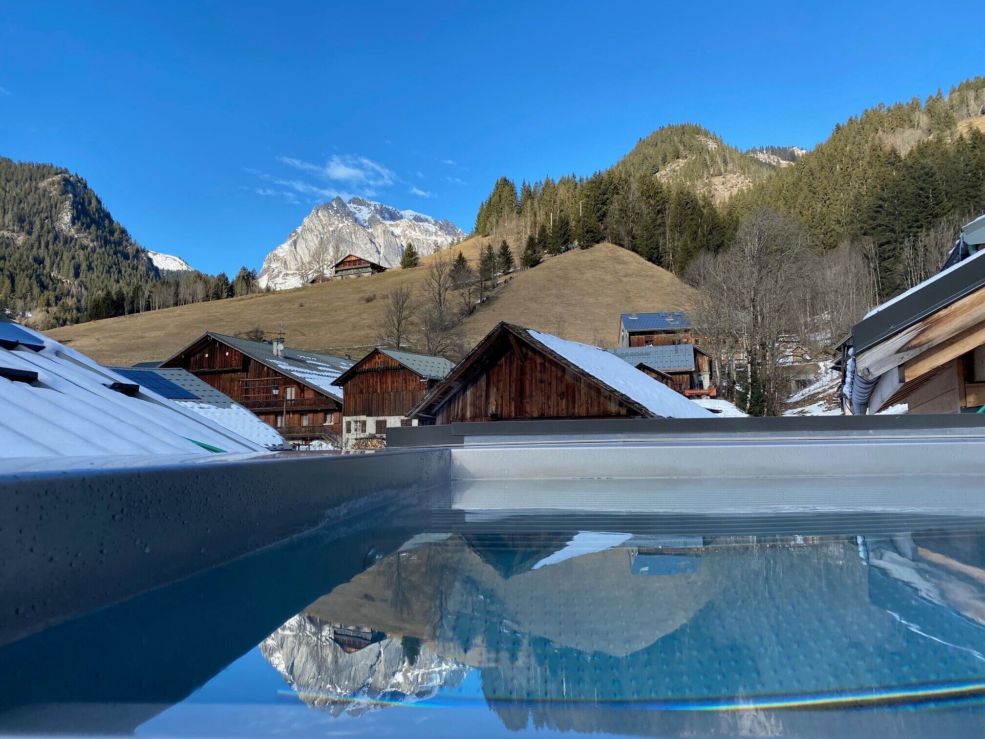Un paysage de montagne avec des chalets en bois et un reflet clair dans une étendue d’eau.