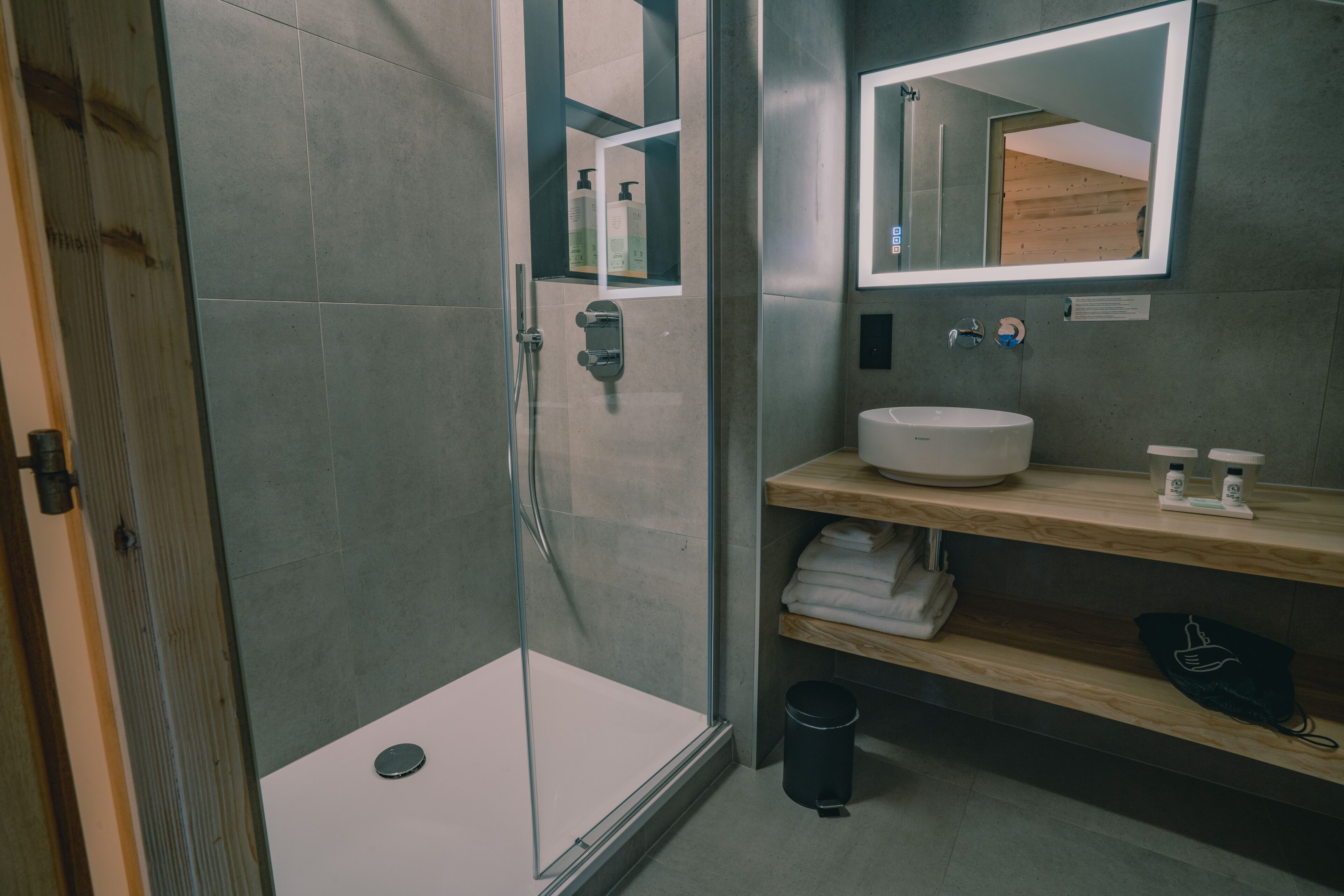 A modern bathroom with a glass-enclosed shower, a white sink, and a wooden vanity.