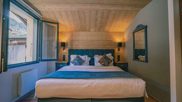 A bedroom with a wooden ceiling, a large bed with white and blue bedding, two bedside tables with lamps, and a large mirror on the wall.