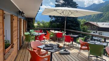 A wooden deck with outdoor seating, including tables and chairs, and a large umbrella providing shade.