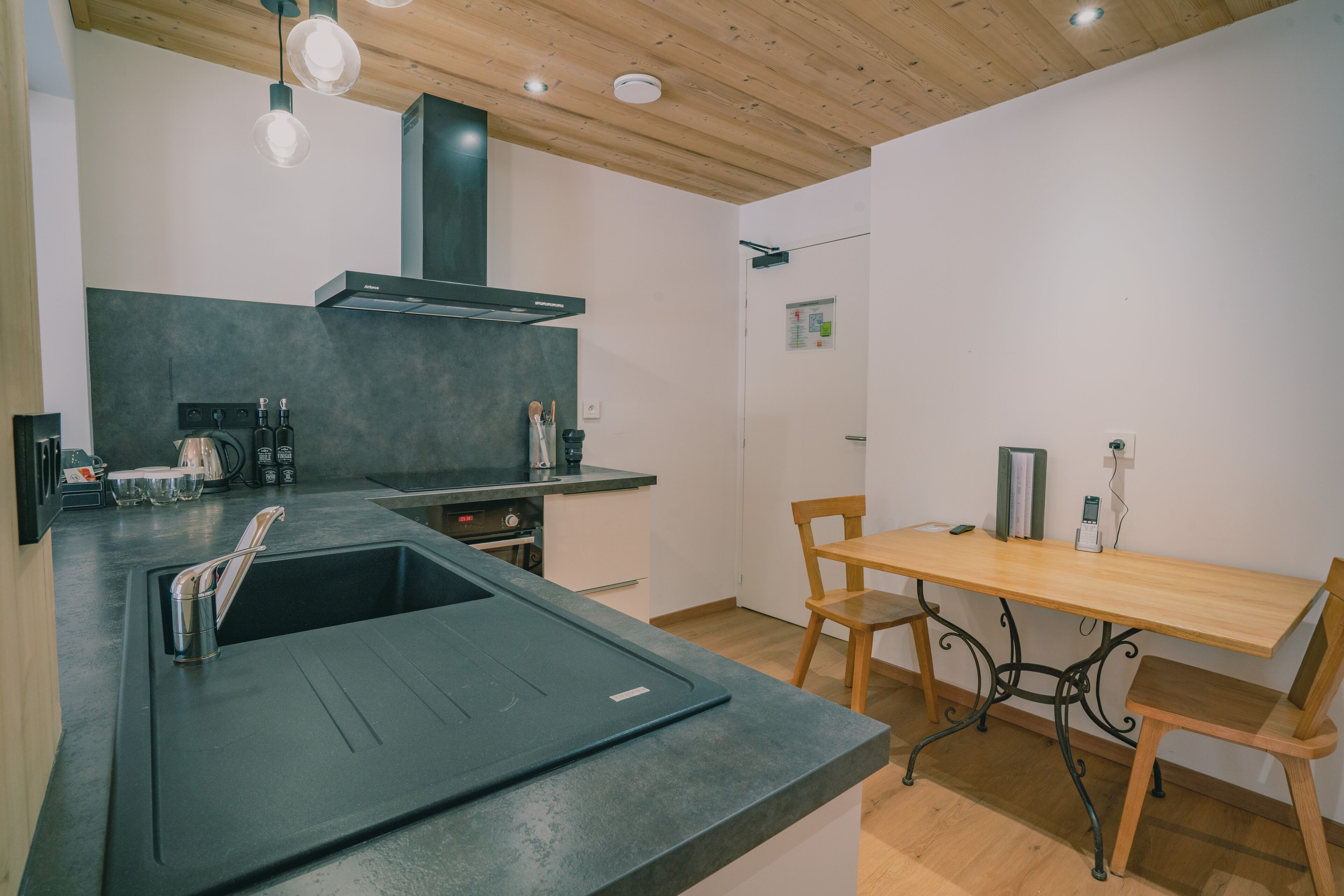 A modern kitchen with a black countertop, stainless steel sink, and wooden dining table with metal legs.